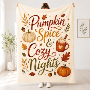 May include: A cream-colored fleece blanket featuring the text "Pumpkin Spice & Cozy Nights" in brown and orange script. The design includes illustrations of two pumpkins, a mug of hot cocoa with a heart, and various autumn leaves in fall colors.