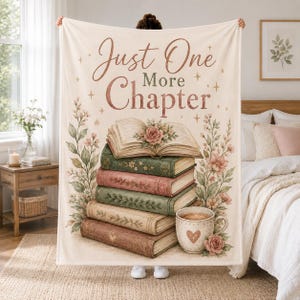 Puede incluir: Una manta de color crema con el texto Just One More Chapter en letra marrón. El diseño incluye una pila de cinco libros de estilo antiguo, un libro abierto con una rosa, enredaderas florales a los lados y una taza con un corazón.