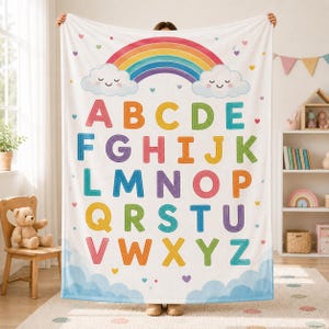 May include: A white fleece blanket featuring a colorful alphabet from A to Z in various bright colors. The design includes a large rainbow arching over two smiling clouds at the top, with small scattered hearts throughout the background.