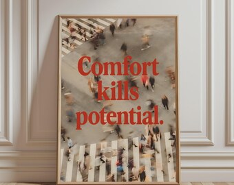 May include: A rectangular framed wall art print featuring a motion-blurred overhead view of people walking across a crosswalk. The text "Comfort kills potential." is printed in bold red serif lettering across the centre of the image.