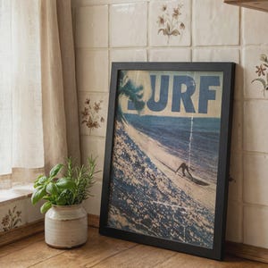May include: A rectangular framed wall art print featuring a vintage-style illustration of a surfer riding a large ocean wave. The word SURF is printed in large blue capital letters across the top. The frame is black and has a simple, clean design.
