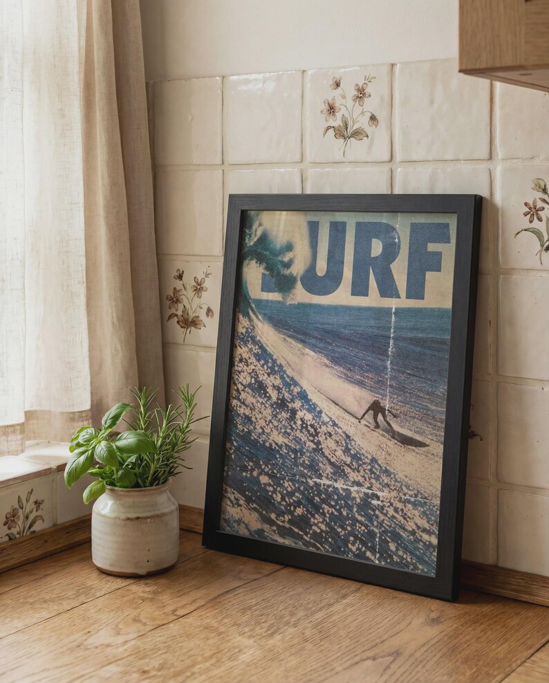 May include: A rectangular framed wall art print featuring a vintage-style illustration of a surfer riding a large ocean wave. The word SURF is printed in large blue capital letters across the top. The frame is black and has a simple, clean design.