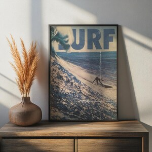 May include: A framed rectangular wall art print featuring a large ocean wave and a surfer riding it, with the word SURF printed in large blue letters across the top. The artwork has a vintage, weathered texture with visible vertical lines.