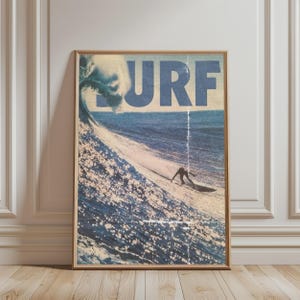 May include: A framed vertical wall art print featuring a large ocean wave and a surfer riding it. The word SURF is printed in large, bold, blue capital letters across the top. The image has a textured, vintage aesthetic with muted blue and tan tones.