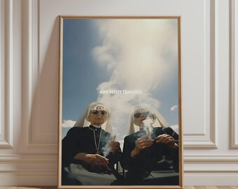 May include: A framed wall art print featuring two individuals dressed in traditional black and white nun habits and sunglasses, each holding a smoking cigarette. The text "nun better than this" is centred in white against a blue sky background.