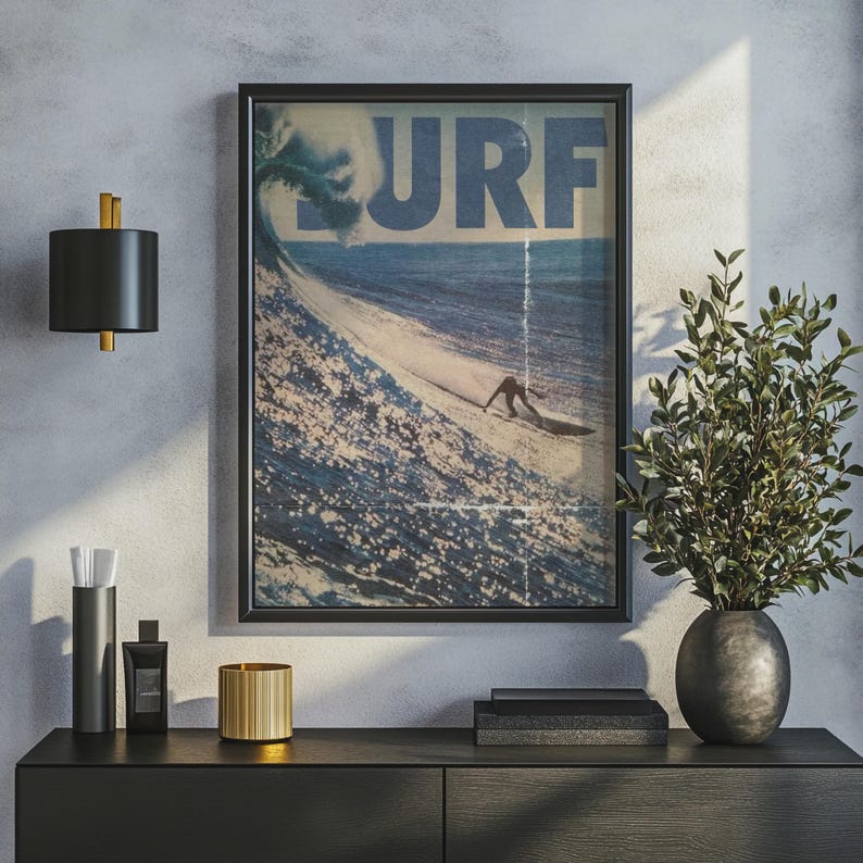 May include: A framed wall art print featuring a vintage-style ocean scene with a large breaking wave and a surfer. The word SURF is printed in large blue letters across the top. The image has a distressed texture with vertical lines.