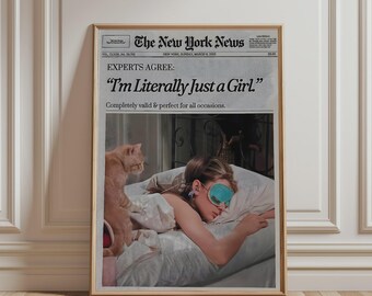 May include: A framed poster featuring a newspaper layout titled The New York News. The headline reads EXPERTS AGREE: I'm Literally Just a Girl. Below, a photograph shows a person wearing a teal sleep mask in bed with an orange cat sitting nearby.