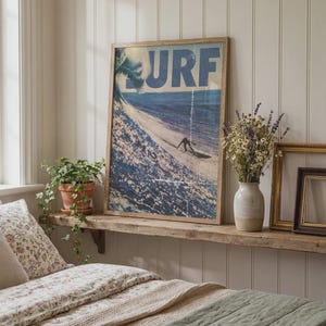 May include: A rectangular framed wall art print featuring a blue ocean wave and a surfer with the text URF in large blue letters at the top. The print is displayed in a light wood frame, showcasing a dynamic scene of a person surfing a wave.