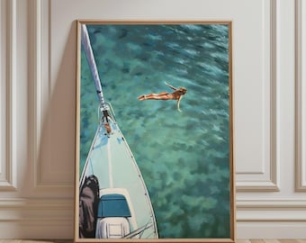 May include: A framed art print depicting a high-angle view of a white sailboat bow cutting through clear turquoise water. A person in a dark bikini is swimming in the sea near the boat. The water shows ripples and light reflections.