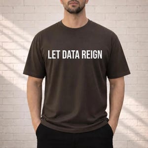 May include: A dark brown short-sleeved t-shirt featuring the white text LET DATA REIGN printed in a clean, sans-serif font across the chest. The garment has a classic crew neckline and a standard fit, providing a simple and direct visual design.