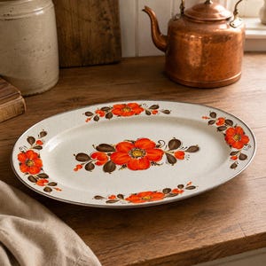 May include: An oval-shaped ceramic serving platter with a speckled off-white base. The platter features a hand-painted floral motif with vibrant orange flowers and dark brown leaves arranged in a central cluster and along the rim edges.