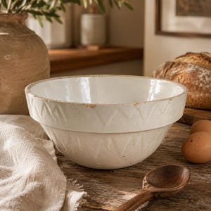 May include: A white ceramic mixing bowl with a wide rim and a subtle embossed zigzag pattern around the exterior. The bowl features a slightly distressed finish with visible brown wear along the top edge, showcasing a classic, functional design.