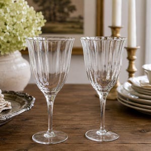 May include: Two clear glass wine glasses featuring a vertical ribbed texture on the bowl, a slender stem, and a circular base. The glasses are made of transparent glass with a fluted design that extends from the rim down to the base of the bowl.