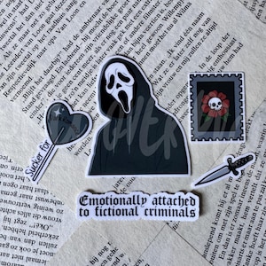 Op de afbeelding: Een set van vijf stickers met een zwart gehulde spookfiguur, een hartvormige lolly met de tekst Sucker for Dark Romance, een postzegel met een schedel en bloem, een zilveren dolk en een banner met de tekst Emotionally attached to fictional criminals.