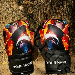 Könnte beinhalten: Ein Paar schwarze Boxhandschuhe mit einem lebendigen Grafikdruck eines Anime-Charakters mit stacheligen blonden Haaren und einem blauen Stirnband. Die schwarzen Handgelenkbänder tragen den weißen Schriftzug "YOUR NAME" auf der Vorderseite.