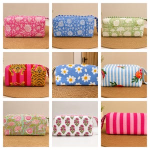 May include: A collection of nine rectangular quilted fabric pouches featuring various patterns including floral prints, tiger motifs, daisy designs, fruit illustrations, and vertical stripes in vibrant colours like pink, blue, green, and white.