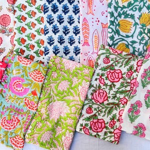 Puede incluir: Una colección de telas de algodón plegadas con varios patrones estampados en bloque, incluyendo flores rosas, motivos florales naranjas y azules, peces naranjas, tulipanes amarillos y diseños botánicos verdes sobre fondos blancos, azul claro y verde lima.
