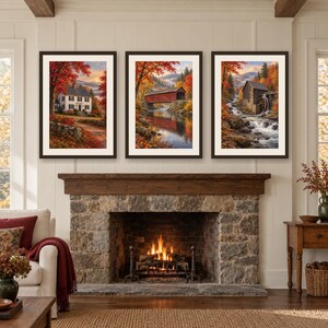 May include: A set of three framed landscape prints displayed above a stone fireplace. The prints feature autumn scenes including a white house, a red covered bridge over a river, and a rustic water mill beside a flowing stream with vibrant foliage.