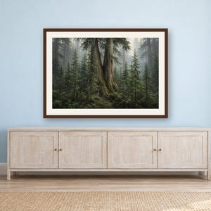 May include: A framed landscape wall art print featuring a dense, misty forest scene with a large, central ancient tree surrounded by smaller evergreen conifers and lush green ferns, all enclosed within a dark brown rectangular frame.