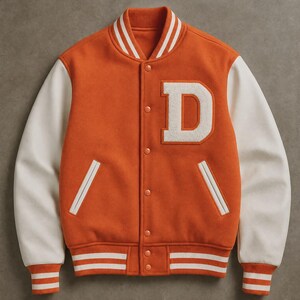 May include: A varsity jacket featuring a vibrant orange body and contrasting off-white sleeves. The front displays a large, white, textured letter D patch on the chest, a snap-button closure, two side pockets, and striped ribbed cuffs and collar.