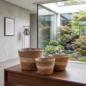 May include: A set of three round woven baskets made of natural brown seagrass fibres, each featuring a distinct horizontal band of lighter, cream-coloured woven material around the middle section and a clear plastic liner inside each basket.