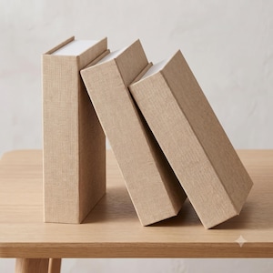May include: Three rectangular storage boxes with a beige linen-textured fabric exterior. The boxes are arranged in a row, with one standing upright and two leaning against it at an angle. Each box features a clean, solid-coloured design.