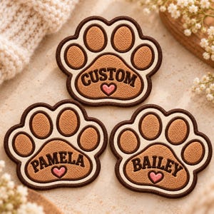 May include: Three embroidered paw print patches with brown and cream stitching. Each patch features a central text area with a small pink heart below the name: CUSTOM, PAMELA, and BAILEY, all outlined in dark brown thread borders.