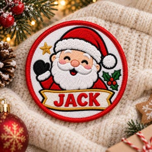 May include: A circular embroidered patch featuring a smiling Santa Claus wearing a red hat and white trim. The patch includes a gold star, green holly leaves with red berries, and a gold banner with the name JACK in bold red letters.