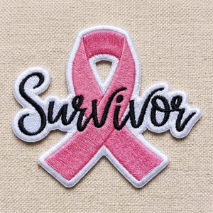 May include: An embroidered patch featuring a pink awareness ribbon with a white border. The word Survivor is stitched in black cursive script across the center of the ribbon. The design is finished with a white outline surrounding the entire shape.
