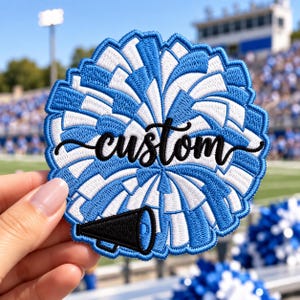 May include: A circular embroidered patch featuring a blue and white cheerleader pom-pom design. The word custom is stitched in black cursive script across the center, and a small black megaphone icon is positioned at the bottom of the patch.