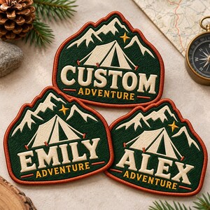 May include: Three embroidered patches featuring a mountain and tent design with a dark green background, cream-colored text, and orange borders. The patches display the words CUSTOM ADVENTURE, EMILY ADVENTURE, and ALEX ADVENTURE in bold lettering.