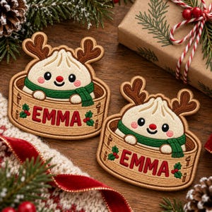 May include: Two embroidered patches featuring a cartoon dumpling character with brown reindeer antlers and a green scarf, sitting inside a tan bamboo steamer basket. The name EMMA is stitched in red letters on the front of each basket.