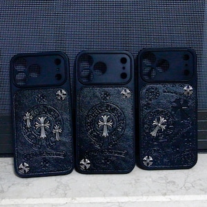 May include: Three black smartphone cases with a textured leather-like finish. Each case features silver-toned metal cross emblems and circular decorative accents embedded into the surface, along with precise cutouts for camera lenses.