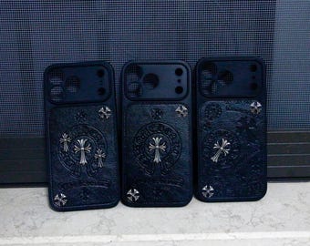 May include: Three black smartphone cases with a textured leather-like finish. Each case features silver-toned metal cross emblems and circular decorative accents embedded into the surface, along with precise cutouts for camera lenses.