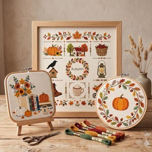 Könnte beinhalten: Drei Kreuzsticharbeiten in Holzrahmen mit herbstlichen Motiven. Ein quadratischer Rahmen zeigt einen Blumenstrauß, Bücher und Kürbisse. Ein großer rechteckiger Rahmen zeigt saisonale Symbole und das Wort Autumn.