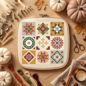 Peut inclure: Un tambour à broder carré en bois contenant un échantillon de point de croix avec neuf motifs géométriques distincts. Les designs présentent une palette de fils jaune moutarde, vert forêt, rouge profond et rose pâle sur un tissu crème.