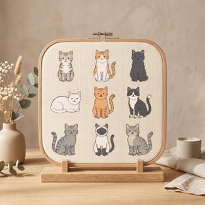 Può includere: Un telaio da ricamo quadrato in legno contenente un motivo a punto croce di nove gatti distinti in vari colori e pose, inclusi motivi tigrati, a tinta unita e bicolore su uno sfondo di tessuto color crema chiaro.