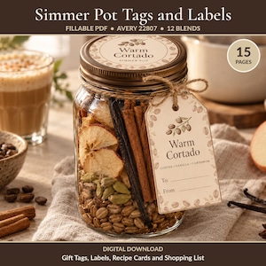 May include: A glass jar filled with dried apple slices, cinnamon sticks, vanilla beans, and cardamom pods. A beige tag tied with twine reads Warm Cortado, Coffee, Vanilla, Cardamom, To, and From. The jar lid has a matching circular label.