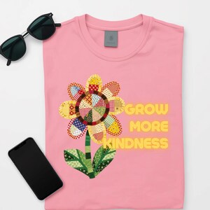 Peut inclure: Un t-shirt rose clair avec un motif de fleur dont les pétales sont composés de divers motifs patchwork colorés. Le texte "GROW MORE KINDNESS" est imprimé en lettres capitales jaunes à droite de la tige et des feuilles de la fleur.
