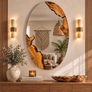 Puede incluir: Un espejo de pared ovalado con un marco de madera natural de borde vivo con detalles de corteza irregulares. El espejo refleja el interior de una habitación, incluyendo una lámpara colgante tejida, un tapiz de macramé, una planta y un sofá.
