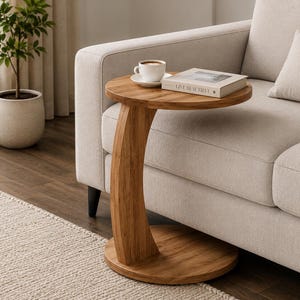 Pu&ograve; includere: Un tavolino a forma di C realizzato in legno marrone chiaro con una base circolare e un piano circolare abbinato. Il tavolo presenta una colonna di supporto verticale curva che collega la base alla superficie superiore, che sostiene una tazza.