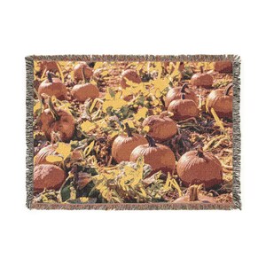 May include: A rectangular woven throw blanket featuring a detailed scene of orange pumpkins resting in a field with dried vines and foliage. The blanket has a decorative fringed edge on all four sides and a textured, tapestry-style weave.