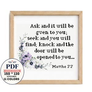 Può includere: Uno schema a punto croce in una cornice di legno chiaro con il testo nero Ask and it will be given to you; seek and you will find; knock and the door will be opened to you... Matthe 7:7 e un motivo floreale viola e verde.