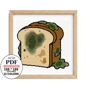 May include: A cross-stitch pattern of a slice of bread with green mold spots, framed in light wood. A circular badge displays the text PDF DIGITAL PATTERN 120 * 130 STITCHES 13 COLORS. The design features brown crust and beige bread interior.