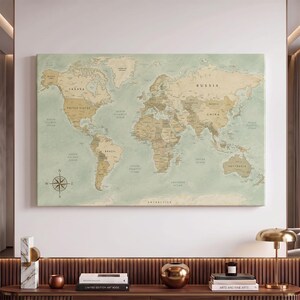 Peut inclure: Une impression murale rectangulaire représentant une carte du monde avec un fond vert sauge atténué et des masses terrestres de couleur beige. La carte affiche les noms des pays, des océans et une rose des vents dans le coin inférieur gauche.
