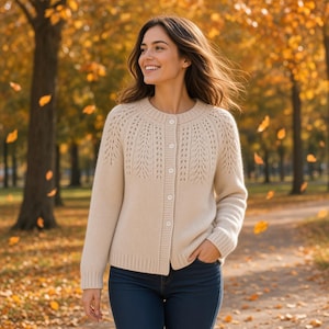 May include: A cream-colored knit cardigan featuring a round neckline, long sleeves, and a button-down front. The upper chest and shoulder areas display a detailed leaf-like lace pattern, while the rest of the garment has a smooth knit texture.