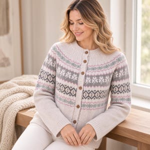 Könnte beinhalten: Eine langärmelige Strickjacke in Cremefarben mit Rundhalsausschnitt und durchgehender Knopfleiste. Das Kleidungsstück ist im Brust- und Schulterbereich mit einem horizontalen Fair-Isle-Muster in zartem Rosa, Salbeigrün und Grau verziert.