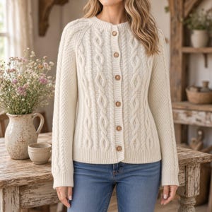 Può includere: Un cardigan color crema a maniche lunghe con un motivo a trecce verticali sul davanti e una lavorazione a maglia testurizzata sulle maniche. Il capo presenta uno scollo rotondo ed è chiuso al centro da sei bottoni rotondi in legno chiaro.