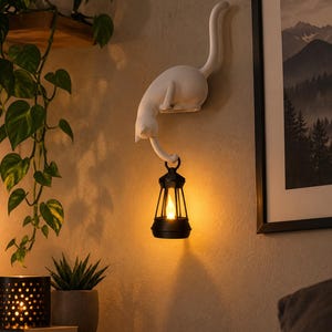 Peut inclure: Une sculpture murale de chat blanc avec le dos arqué et la queue dressée. La patte avant du chat s'étend vers le bas pour tenir une lanterne noire qui émet une lumière chaude et brillante depuis une ampoule en forme de flamme sur le mur.