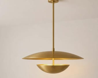 May include: A brass pendant light fitting featuring a central vertical rod connected to a wide, flat, circular upper disc and a smaller, bowl-shaped lower component. The metal has a smooth, brushed finish, and the design is symmetrical.